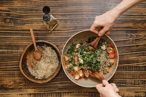 Hands gently mix fresh tomatoes, herbs, and chopped walnuts in a large bowl. Wine vinegar oil is