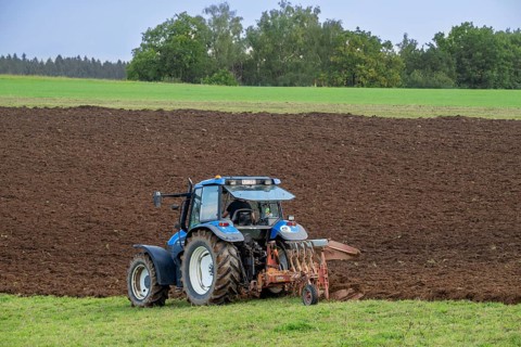 Tractor with plough, agricultural ploughing machine working on a field in autumn, fall in the