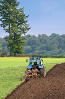Tractor with plough, agricultural ploughing machine working on a field in autumn, fall in the