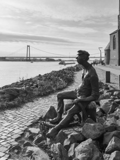 Black and white photo bronze sculpture Poortekerl looking at ships on Rhine Rhine Rhine river