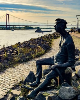 Photo with melancholy mood of bronze sculpture Poortekerl looking at Rhine waiting for ship to