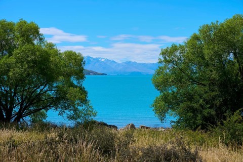A lake surrounded by trees in the foreground, with a spectacular mountain backdrop and clear blue