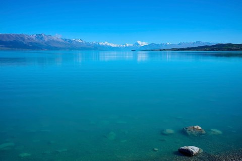 Clear, calm lake in front of a distant mountain range under blue sky, Lake Pukaki Viewpoint,