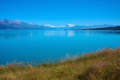 View over grassy banks to the mountain range behind the lake, Lake Pukaki Viewpoint, Pukaki,
