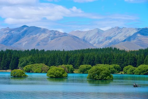 A lake with small green islands and wooded slopes against a mountain range and blue sky, Lake