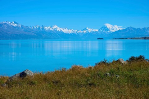View over grassy shores to mountains across the lake, Lake Pukaki Viewpoint, Pukaki, Canterbury,