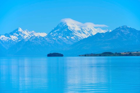 Large snow-capped mountain Mount Cook over a calm blue lake with a small island, Lake Pukaki