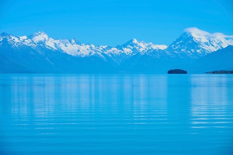 Expansive view of a tranquil lake with snow-capped mountains Mount Cook and an island, Lake Pukaki