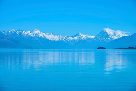 Mount Cook snow-capped mountains are reflected in a calm, blue lake, Lake Pukaki Viewpoint, Pukaki,