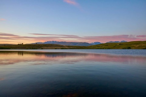 Lake with calm water and mountains in the background with a pink-blue sky, Lake McGregor, Tekapo,