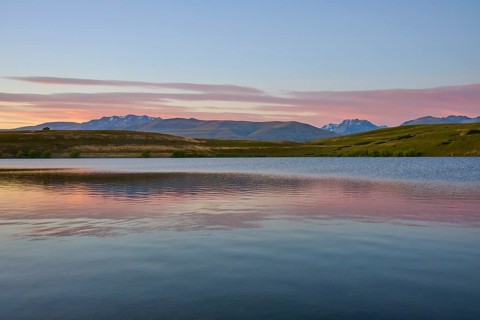Clear lake with mountains in the background under a pink-blue morning sky, Lake McGregor, Tekapo,