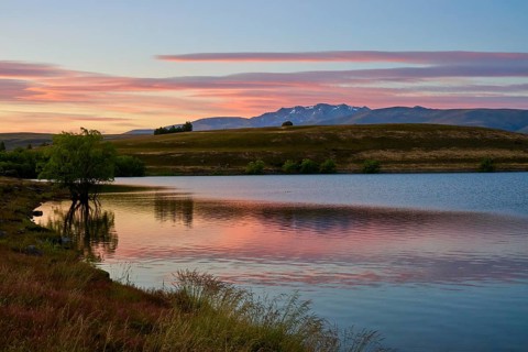 Reflecting lake with mountains in the background at sunrise with pink sky, Lake McGregor, Tekapo,