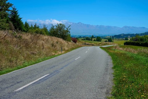 Empty country road leads through green landscape with distant mountains, Geraldine Fairlie Lookout,