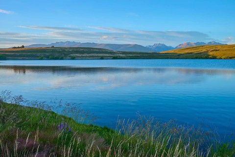 Calm lake with surrounding mountains and blue sky at sunset, Lake McGregor, Tekapo, Canterbury,