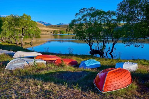 Boats on the shore of a calm lake at dusk with reflecting mountains in the background, Lake
