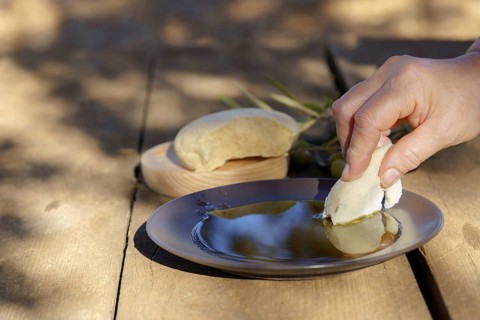 Hand dipping fresh homemade bread into healthy extra virgin olive oil, a staple of homemade