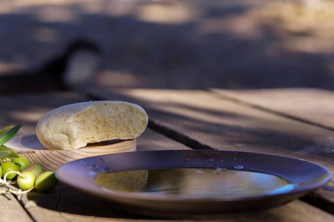 Extra virgin olive oil in a bowl, bread, and green olives on a rustic wooden table capturing