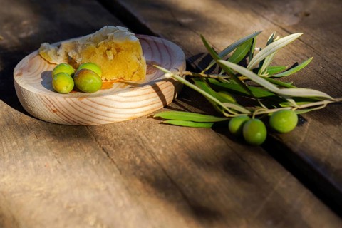 Freshly picked green olives, an olive branch, and rustic bread on a wooden surface, suggesting