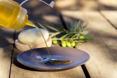Pouring fresh extra virgin olive oil from a squirt bottle onto a plate, with olive branches in the
