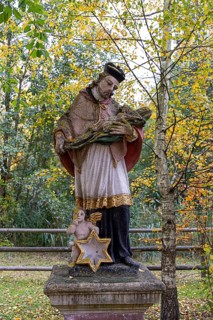 Religious statue with cape and angel in an autumnal park in front of yellow leaves, Weinviertel