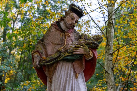 Close-up of a religious statue with a cape in an autumnal park, covered by moss, Weinviertel Lower