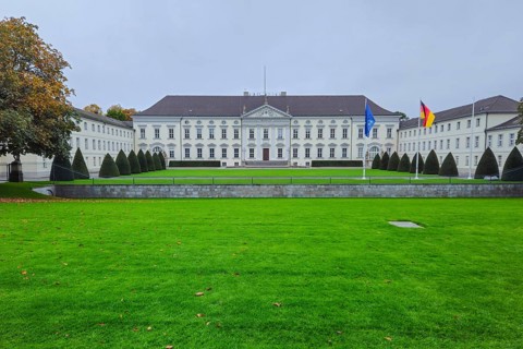 Neoclassical castle in front of a well-kept lawn, lined with topiaries, under grey skies with