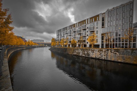 Modern apartment block on the river with yellow autumn trees, dramatic sky reflected in calm water,