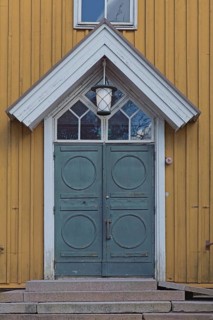 Closed old decorative double doors with white frame and window on top on a yellow board wall,