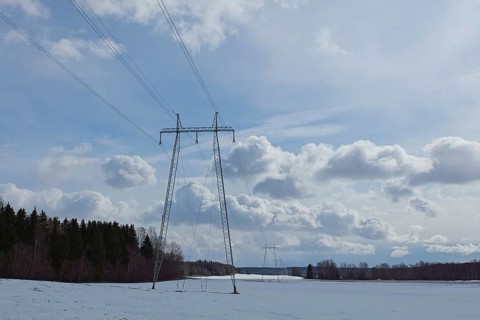 Steel tower with high voltage electric lines in cloudy winter weather with snow on the ground,