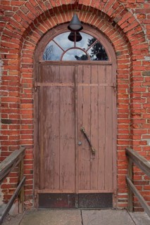 Closed old brown double doors with arch window on top on a red brick wall, Karjalohja, Finland