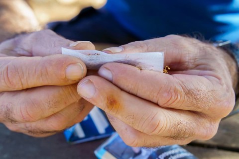 Close-up of hands with yellow stained fingers rolling tobacco into a cigarette, showing a smoking
