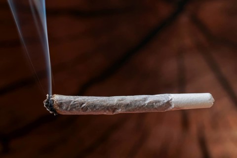 Burning joint producing smoke, highlighting drug use, cannabis culture, addiction, and illegal