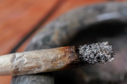 Close-up of a burning cigarette with a long ash resting on a dirty ashtray, symbolizing an
