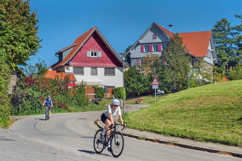 Country road with S-curve and two cyclists in Maria-Thann, Allgäu, Swabia, Bavaria, Germany