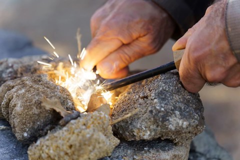 Bushcraft survivalist creating fire sparks with a ferro rod and cotton tinder, gathering heat