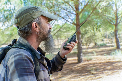 Man with beard and cap holding a walkie-talkie, communicating during an outdoor activity in a