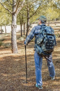 Man walking an outdoor path, carrying a camouflage backpack and trekking pole, enjoying nature and