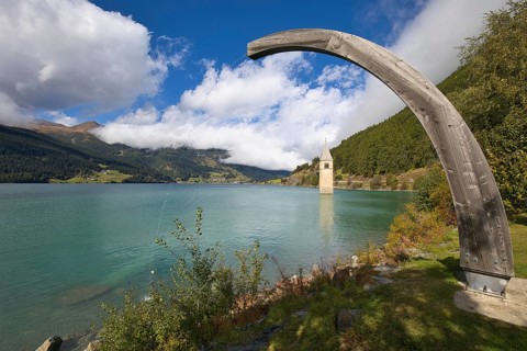 Old Grauner church tower in Lake Resia under a wooden arch in Vinschgau, Italy