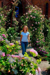 Blonde young beautiful woman walking among roses in the Rosary at the monastery in Ystad, Skåne