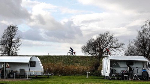 Caravan and motorhome on a campsite, a cyclist drives across the dike on the Baltic Sea, Fehmarn,
