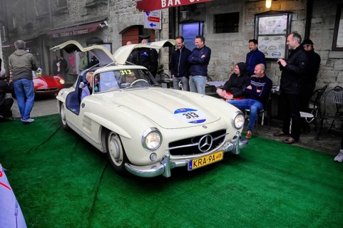Creamy white 300 SL with open double doors poses on the green carpet, surrounded by smiling