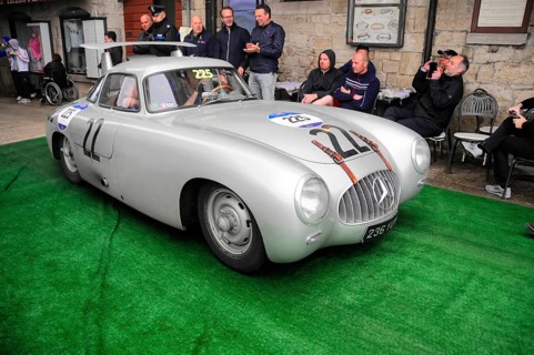 Silver Mercedes gullwing door with race number in a narrow alley at a classic car rally, spectators