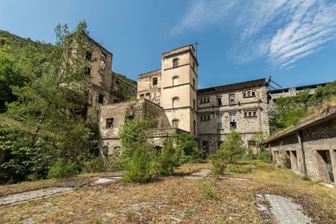 Abandoned building overgrown by vegetation under blue sky, showing signs of weathering and