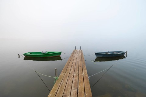 Two boats are moored on a wooden dock in a foggy lake, quiet and peaceful atmosphere, Hopfensee,