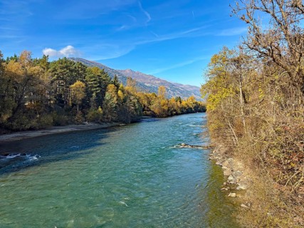 A quiet river surrounded by autumn trees and mountains under clear blue skies, Drau, Drauradweg,
