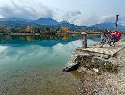 An idyllic lake with a bicycle on a jetty, surrounded by autumnal landscape and mountains, Drau,