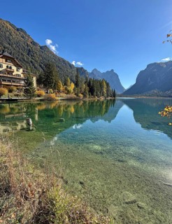 Clear water reflects the mountains and the house on the shore, Lake Toblach, Lake Dobbiaco, South