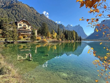 Clear water reflects the surrounding mountains and trees, a house on the shore, Lake Toblach, Lake