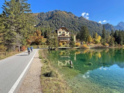 Idyllic autumn scene with a clear lake surrounded by trees and mountains, cyclists on a narrow