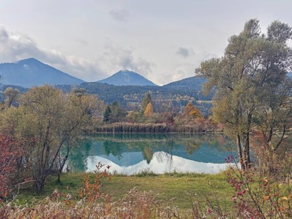 A lake in autumn surroundings, surrounded by mountains and trees under an overcast sky, Drau,